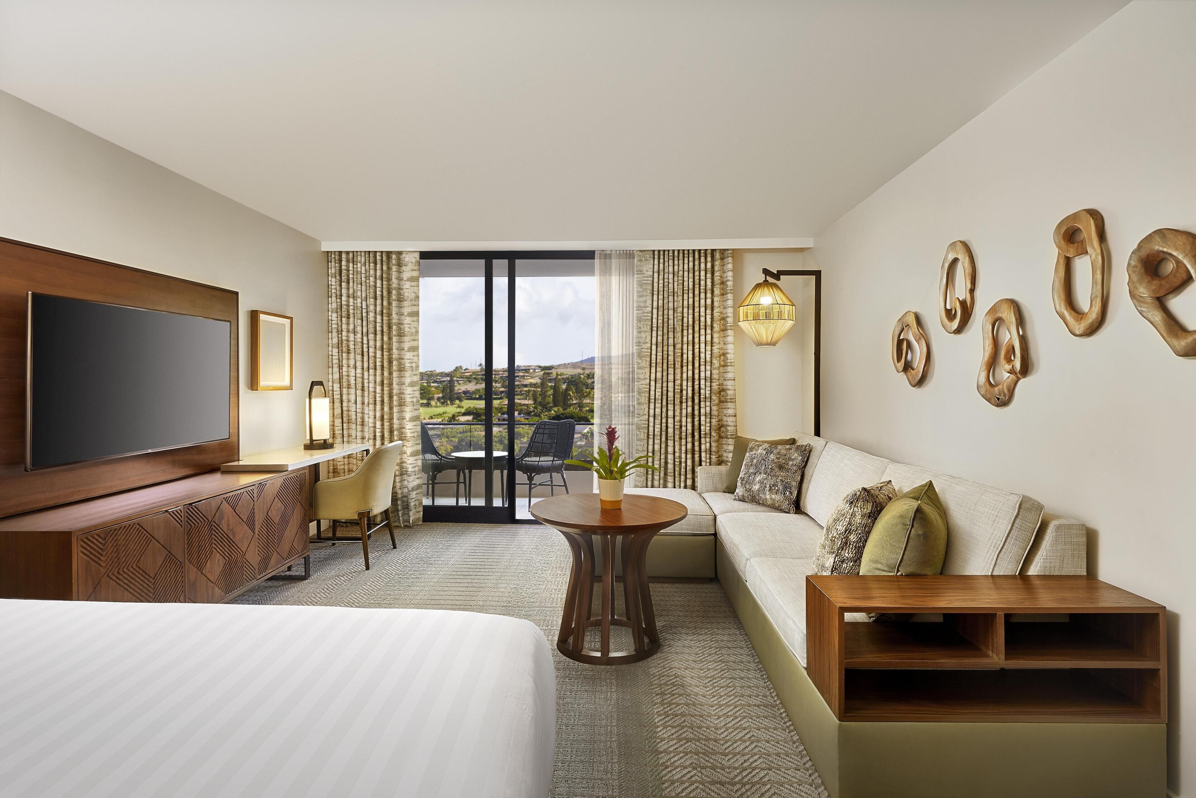 Habitación de hotel con una cama grande, un sofá, un televisor, un escritorio y un balcón con cortinas.