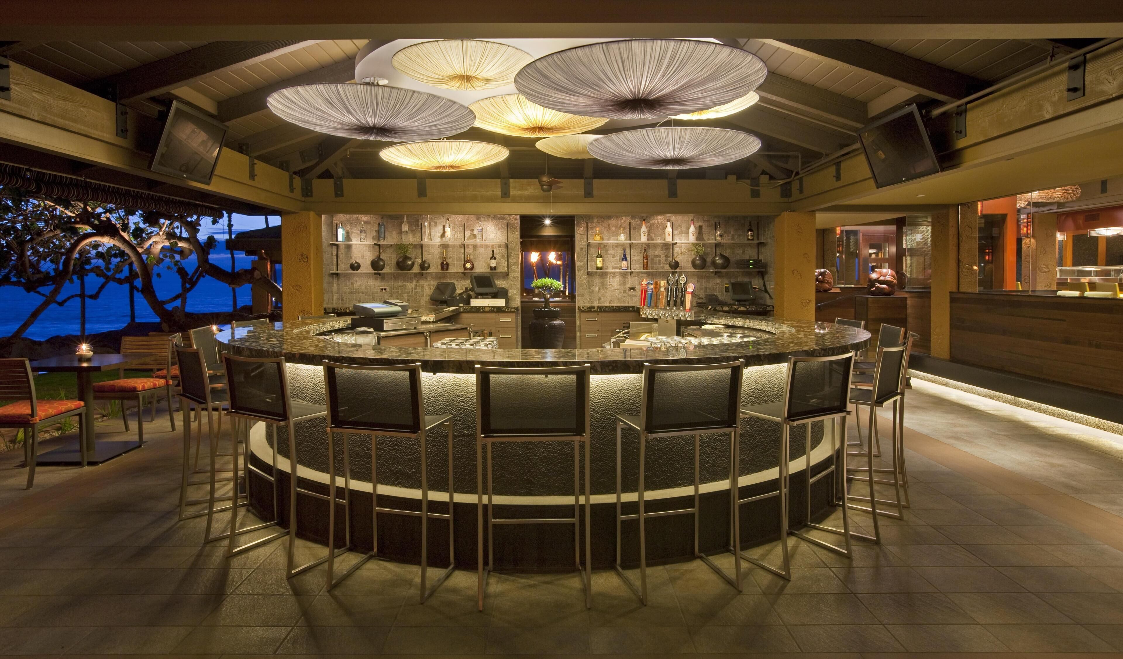 A bar area with a round counter, multiple stools, and overhead lighting fixtures.