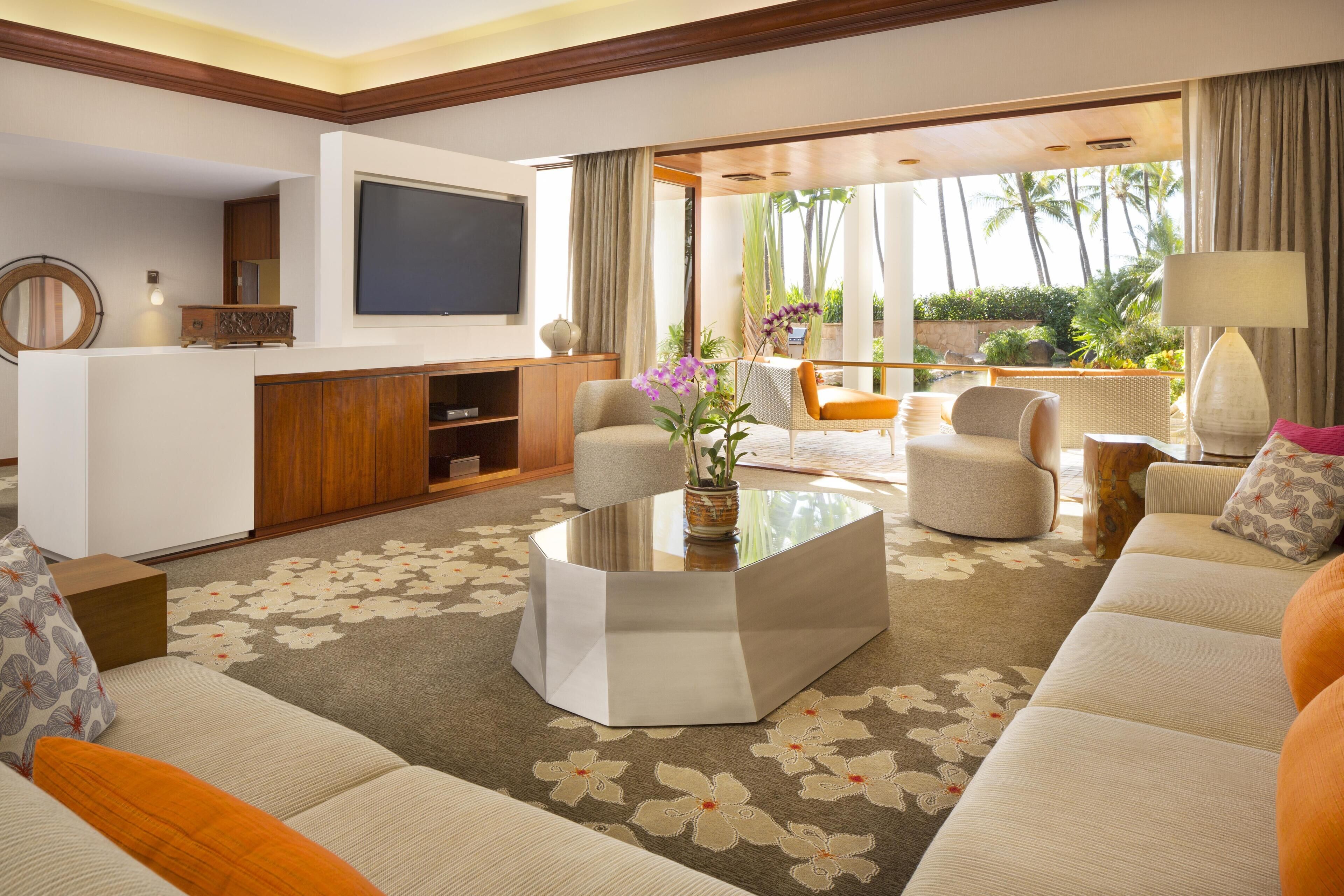 Uma sala de estar moderna com televisão de tela plana, assentos confortáveis, uma mesa de centro e vista para uma área externa tropical.