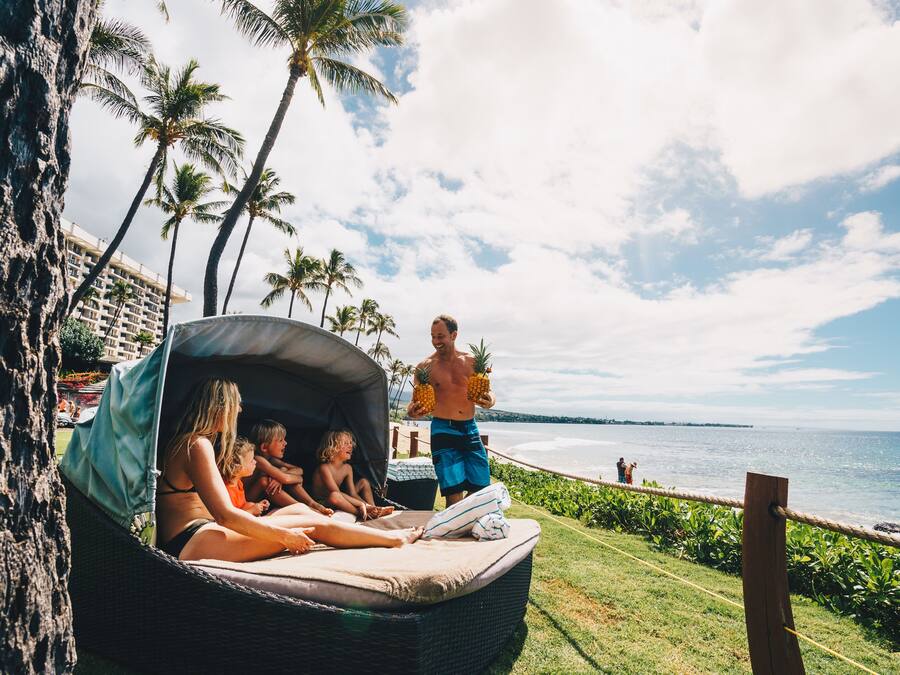 A beachside lounge with a wicker sofa, palm trees, and a view of the ocean.