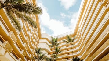 A multi-story hotel atrium with a central open space surrounded by balconies and palm trees.