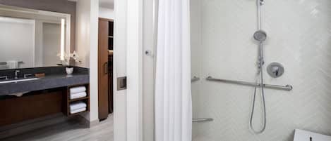 Un baño moderno con ducha, tocador con espejo y un perchero para toallas.