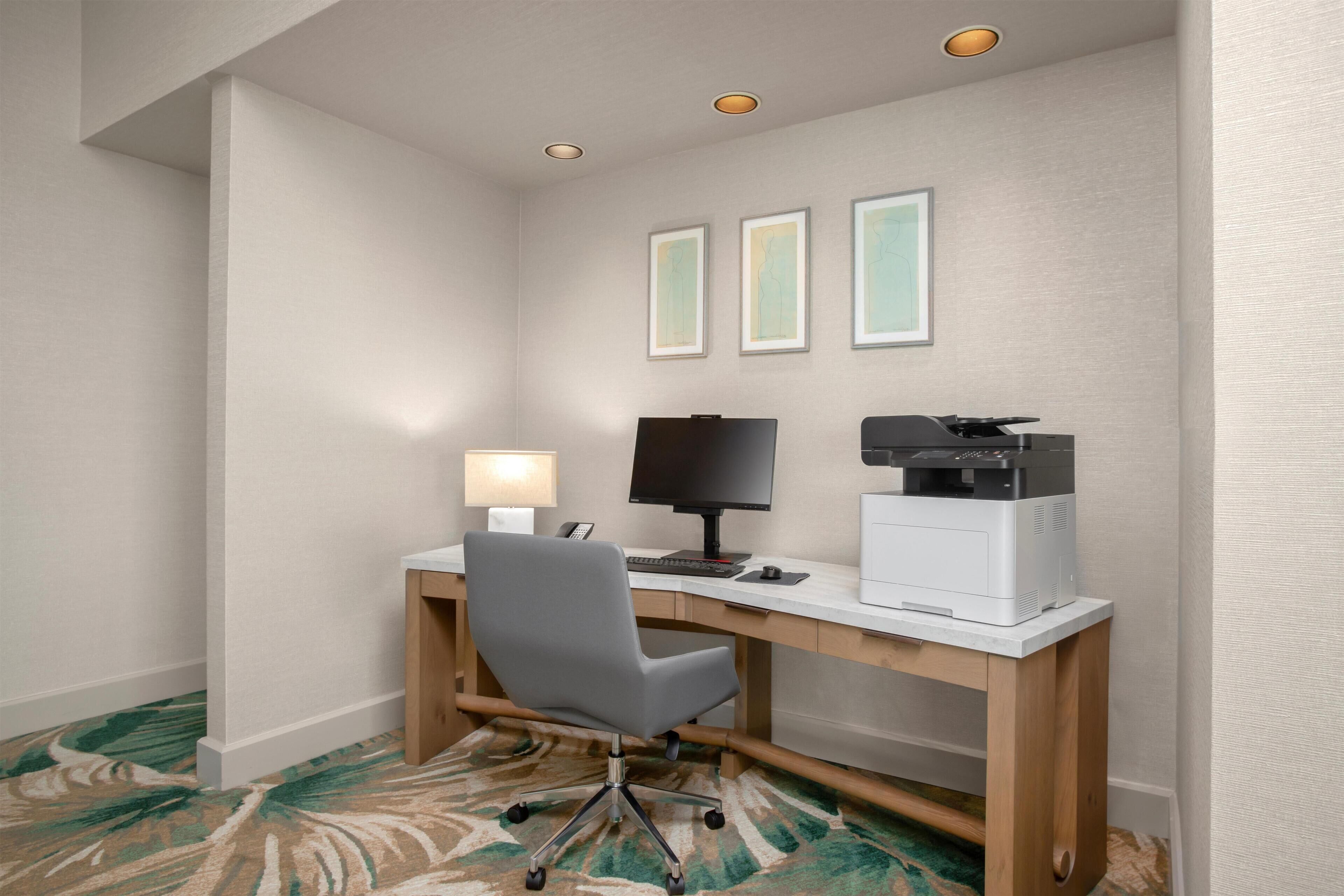 Habitación de hotel con escritorio, silla, computadora, impresora y lámpara.