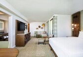 A hotel room with a bed, a TV, a seating area with a sofa and chairs, and a small table.