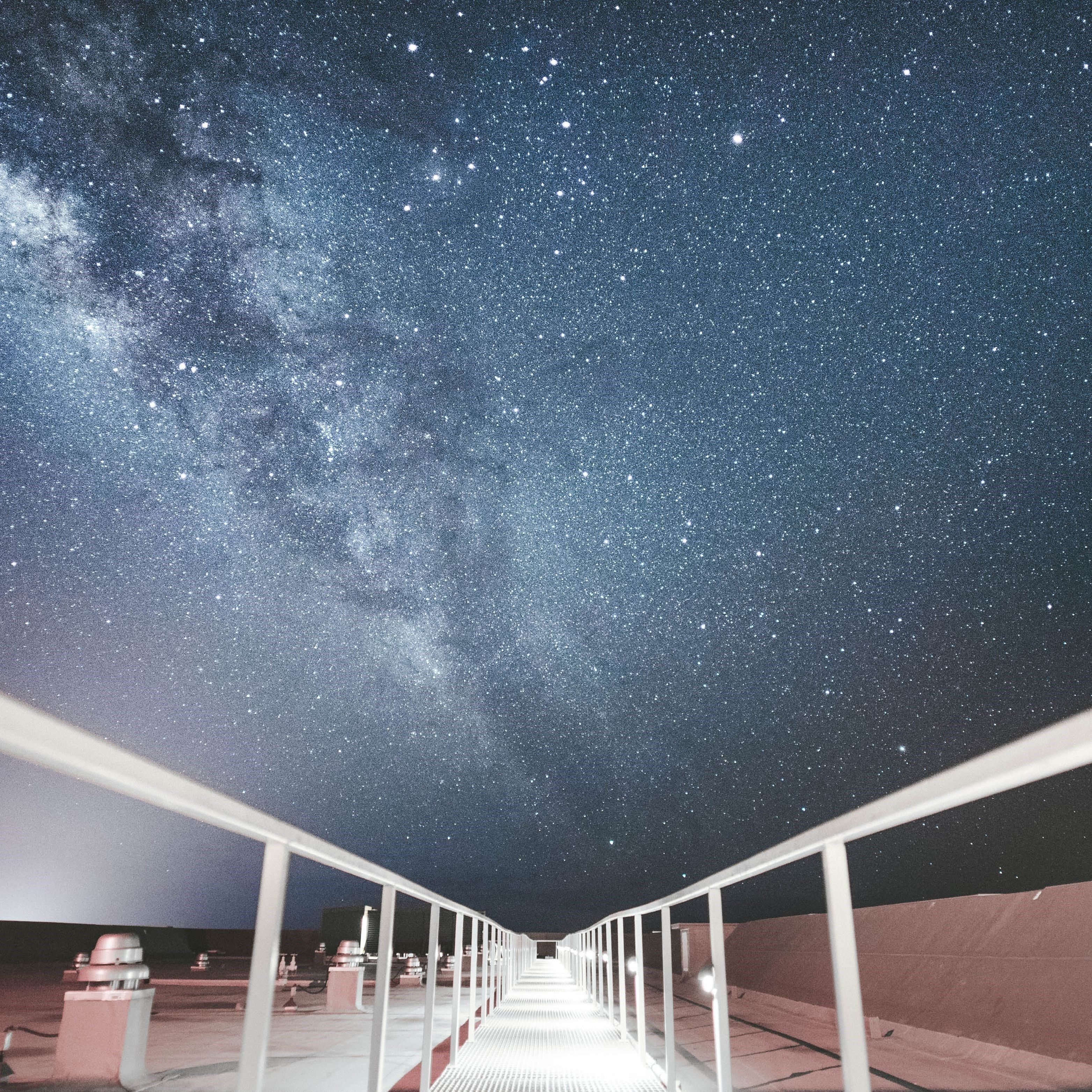 A night sky filled with stars above a long, straight walkway with white railings.