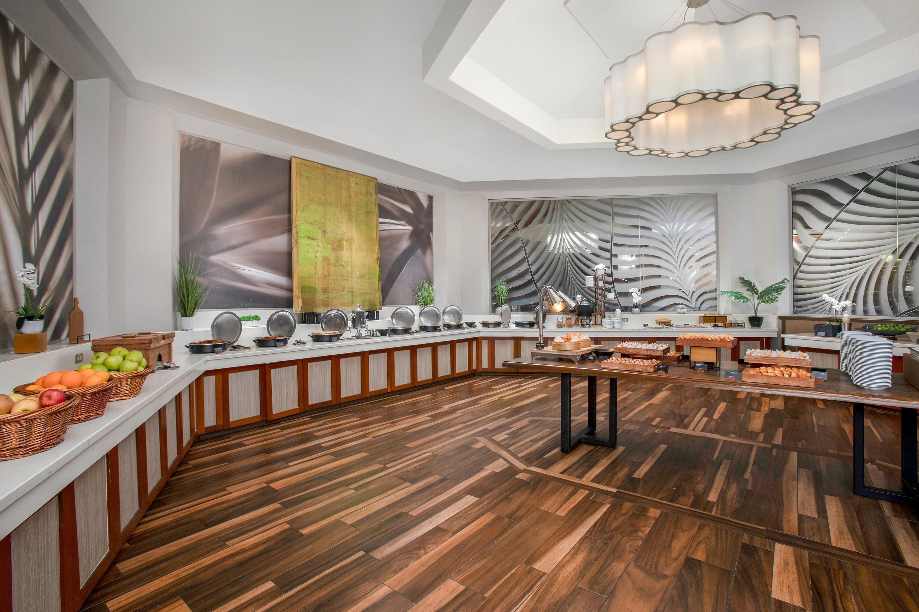 A modern kitchen with a wooden floor, a buffet setup, and a large window.