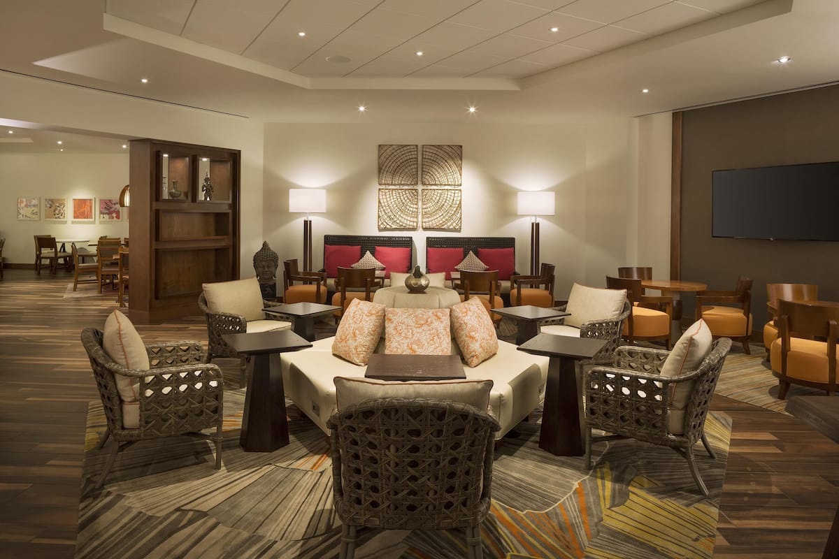 A hotel lobby with a seating area, tables, and a large screen.