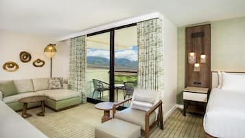 Habitación de hotel con sofá, una mesita, una silla, cama y balcón con vistas a las montañas.