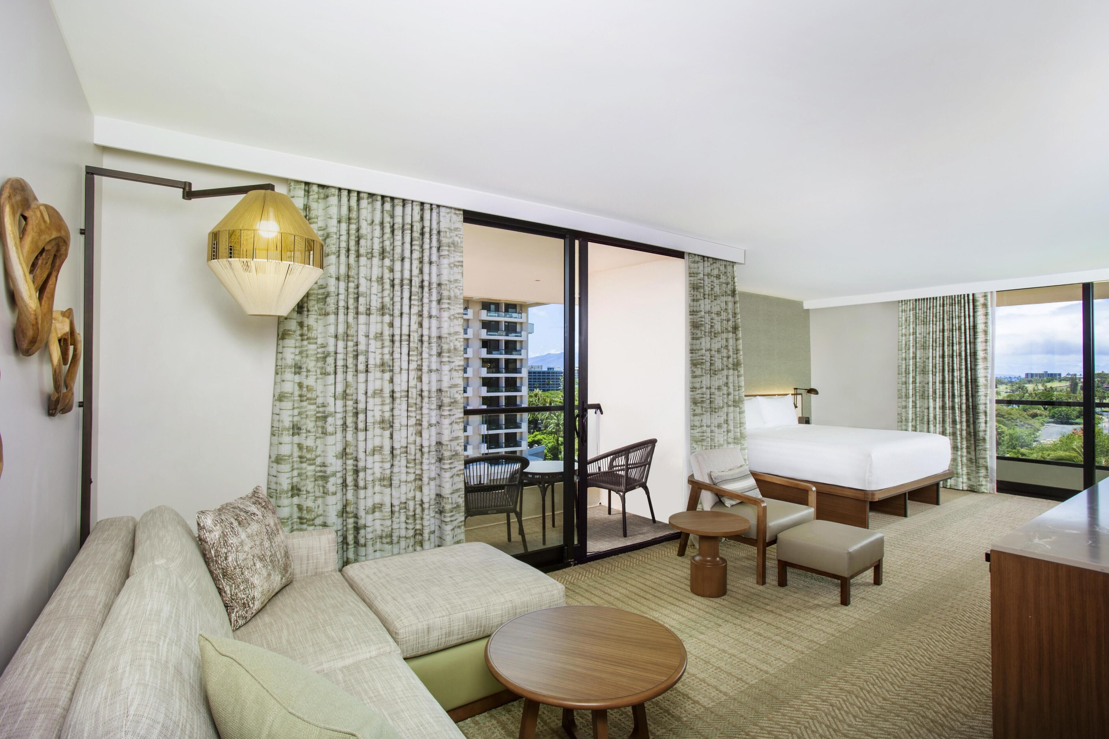 Habitación de hotel con cama, sofá, mesa de comedor y vista a la ciudad.