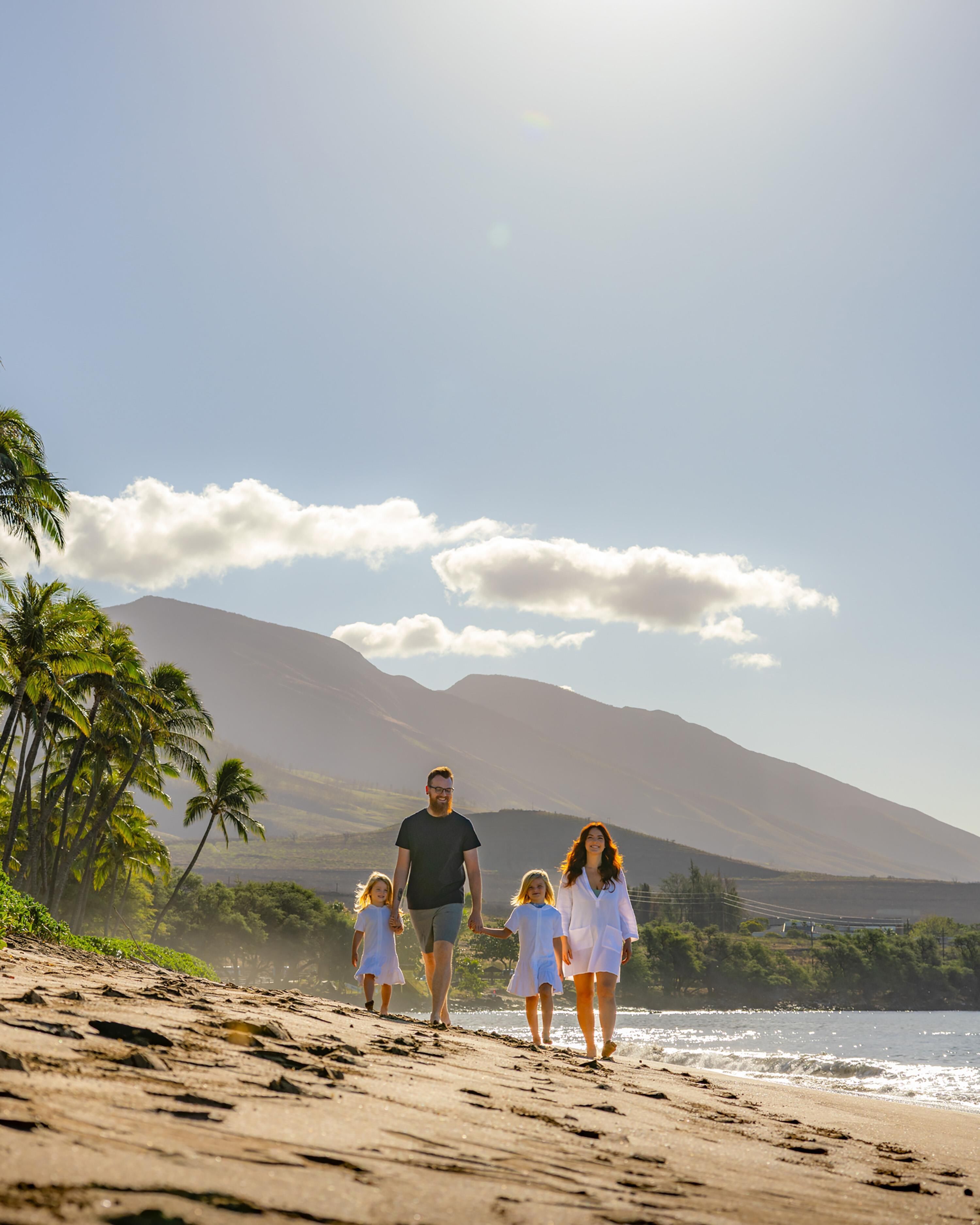 Eine Familie spaziert am Strand, im Hintergrund Palmen und Berge.