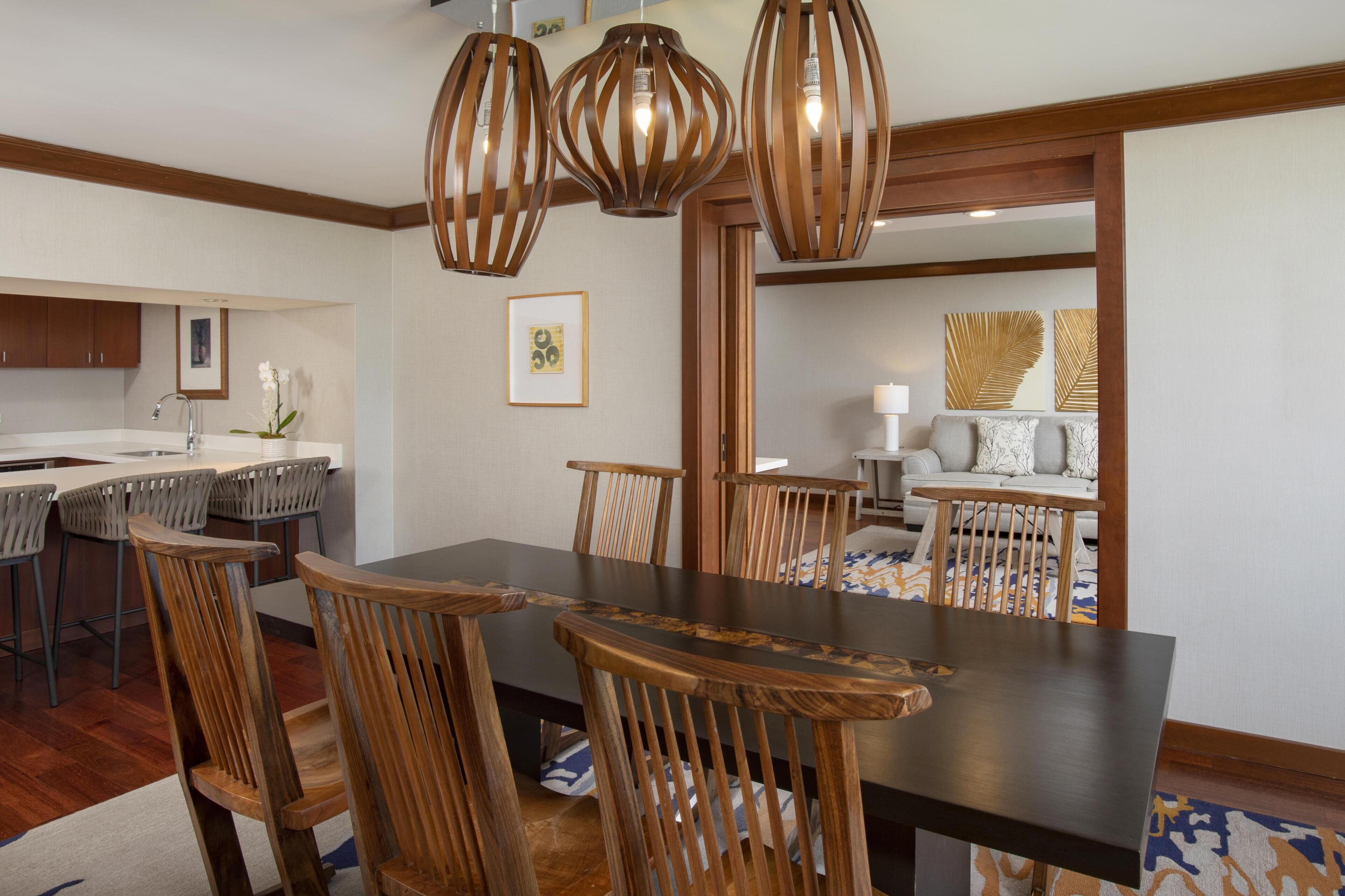 A dining area with a dark wooden table, six wooden chairs, and three hanging pendant lights.