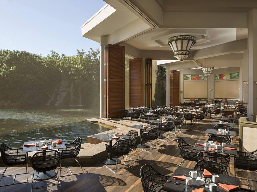 An outdoor dining area with tables and chairs, a pool, and a view of trees.