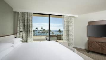 A hotel room with a large bed, a TV, and a balcony with a view of the ocean.