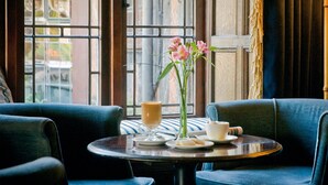 A cozy seating area with a table set for two, featuring a vase with flowers, a cup, and a glass of coffee.
