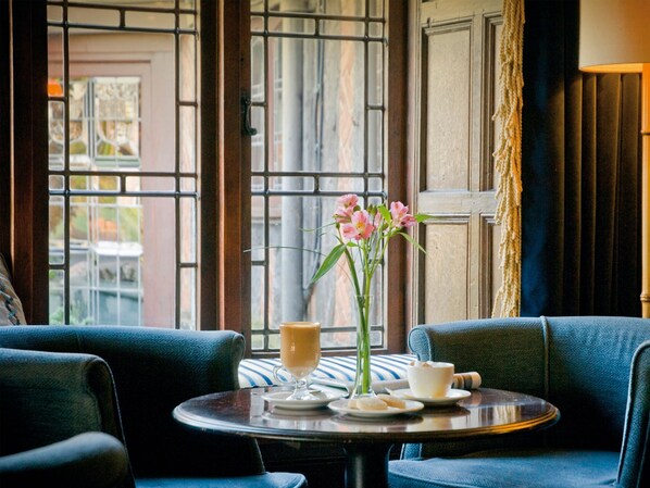 A cozy seating area with a table set for two, featuring a vase with flowers, a cup, and a glass of coffee.