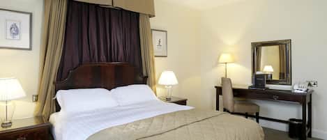 A hotel room with a large bed, two bedside tables with lamps, a desk with a chair, a mirror, and a picture on the wall.