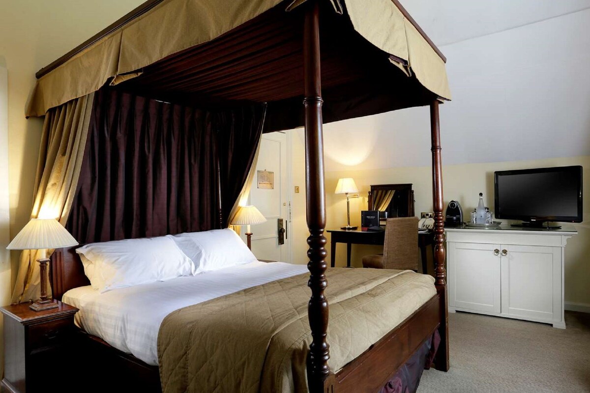 Een hemelbed met baldakijn, een bureau met computer, een televisie en een kast.