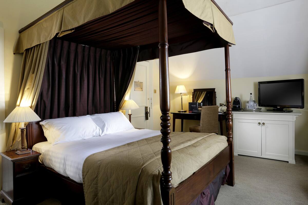 Una cama con dosel, televisor, escritorio y mueble en una habitación de hotel.