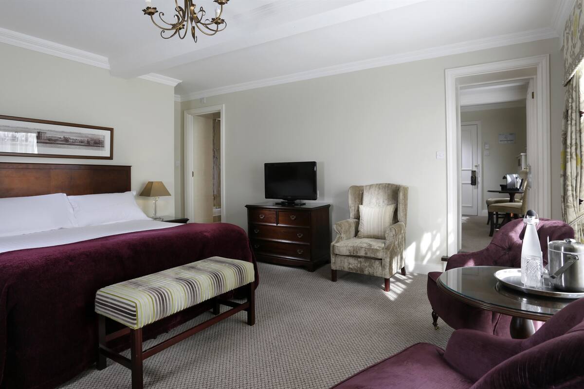 Habitación de hotel con una cama grande, televisión, una silla, un banco y una mesa con bandeja.