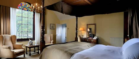 A traditional four-poster bed with a canopy, a large window with stained glass, a chandelier, and a classic wooden chair.