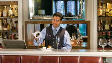 Zona de bar con un cantinero, una copa de vino y una botella de licor.