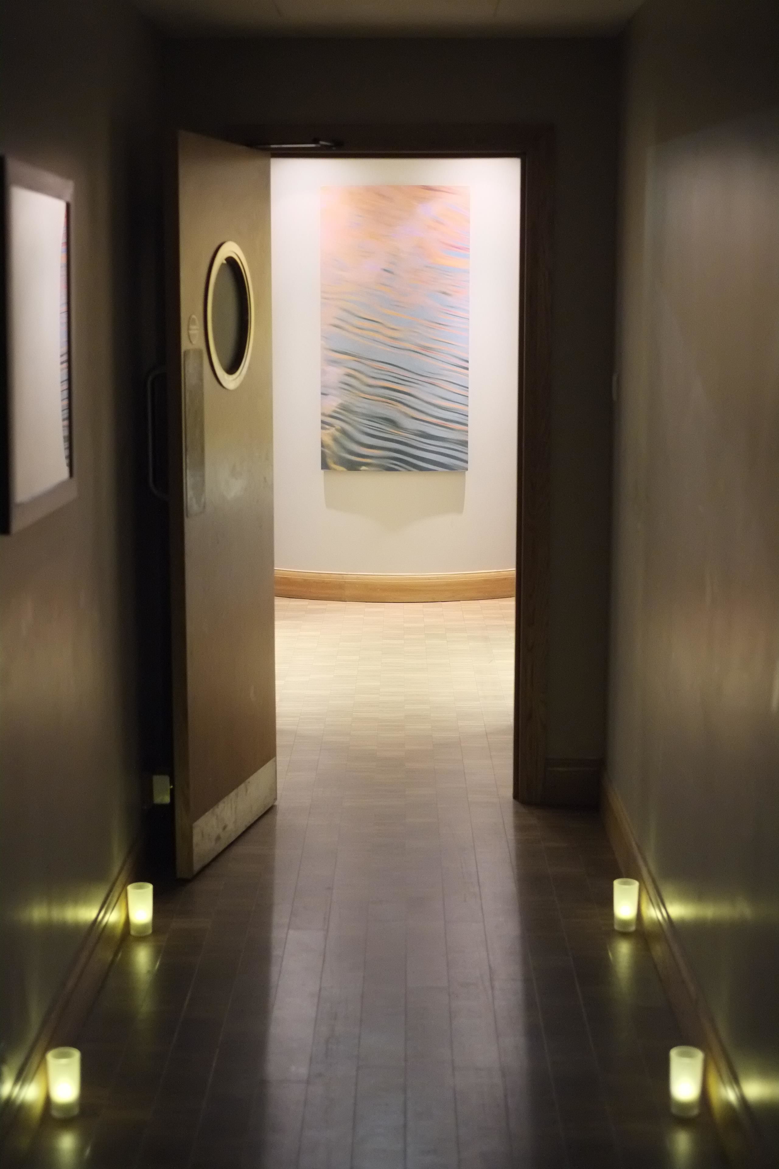 A hallway with a wooden floor, a round mirror on the left, and a painting on the wall.