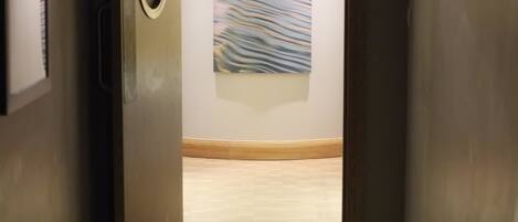 A hallway with a wooden floor, a round mirror on the left, and a painting on the wall.