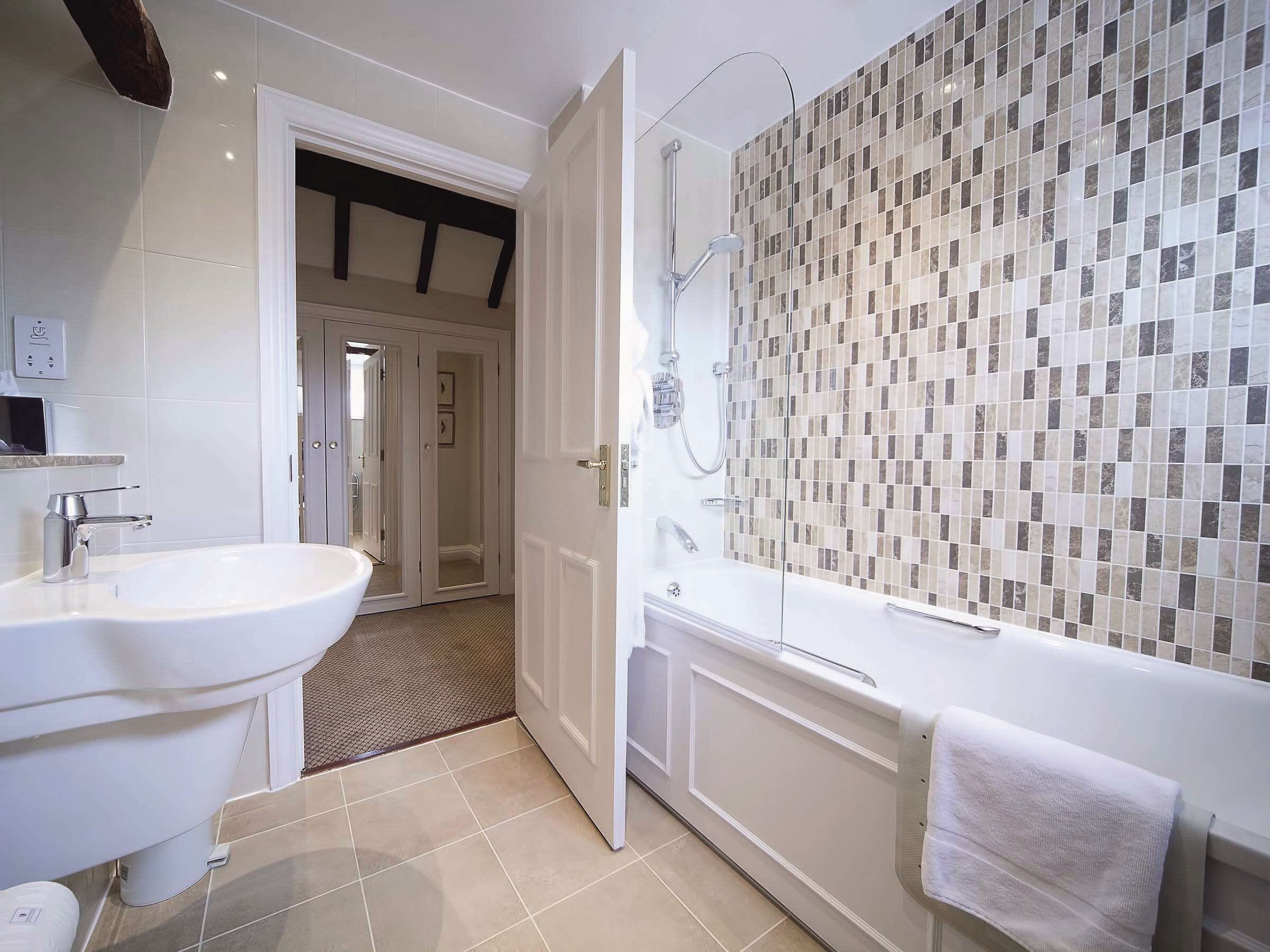 A modern bathroom with a large white sink, a glass-enclosed shower, and a mosaic-tiled wall.