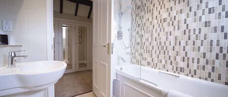 A modern bathroom with a large white sink, a glass-enclosed shower, and a mosaic-tiled wall.