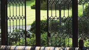 A room with a view through a window with metal bars, a striped sofa, and a lamp in the background.