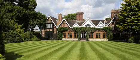 A large, traditional house with a well-maintained lawn, brick chimneys, and a symmetrical facade.