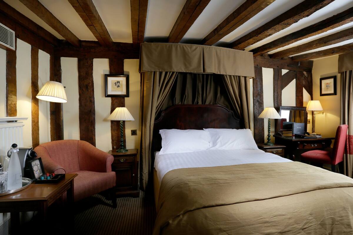 Habitación de hotel con una cama grande, un escritorio con lámpara, una silla y una mesita de noche.