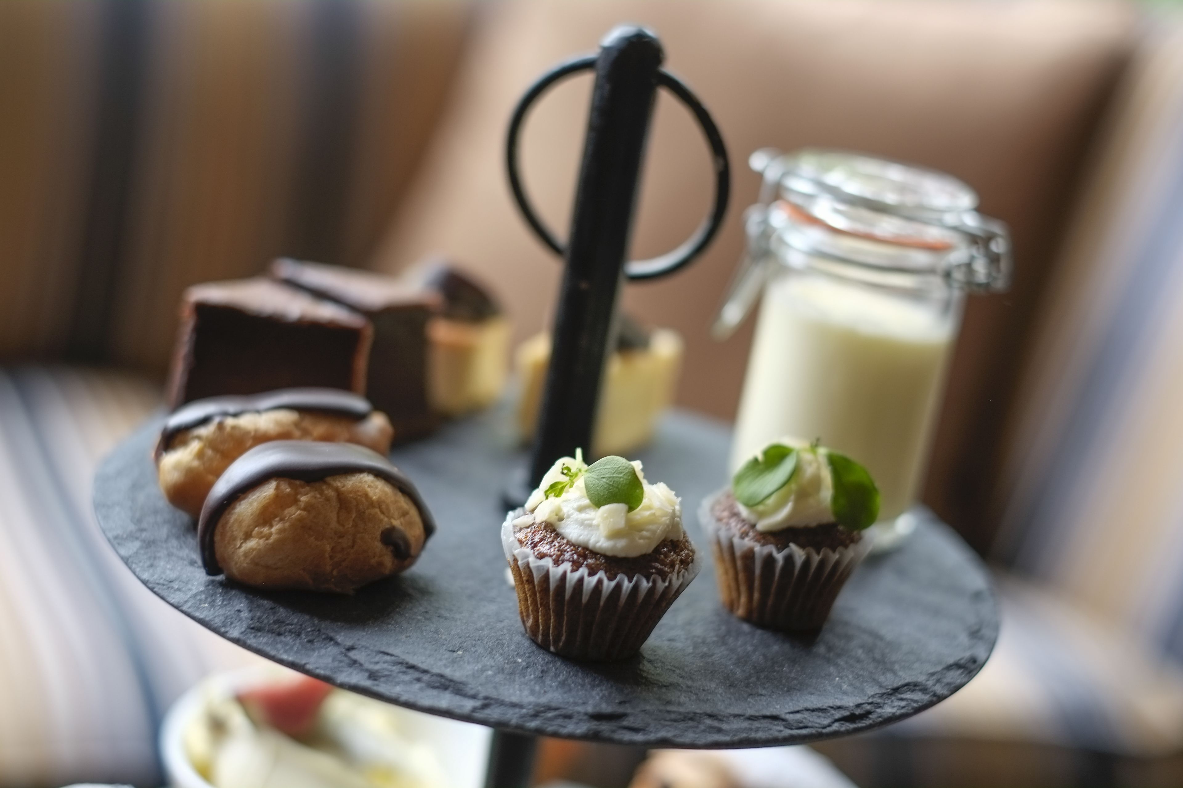 A dessert display with various pastries and a glass jar of milk on a slate serving board.