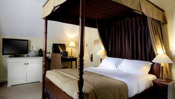A four-poster bed with a canopy, a desk with a computer, a television, and a lamp.
