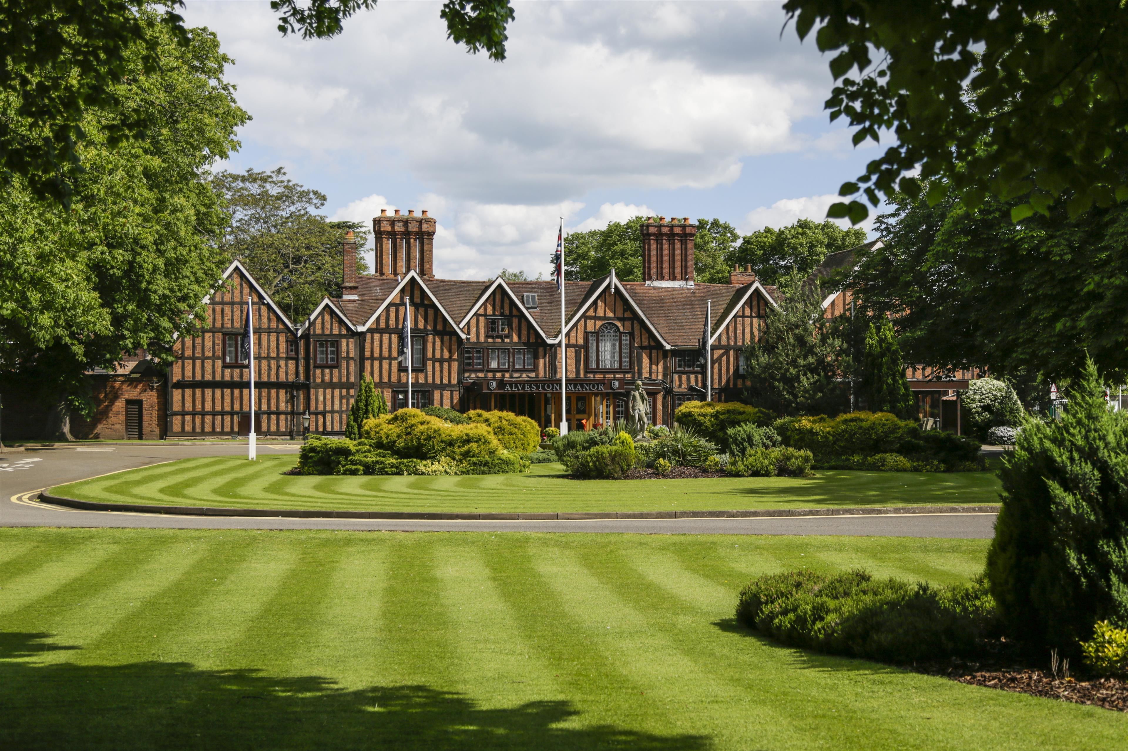 A traditional Tudor-style building with a well-maintained lawn and a statue in the front.