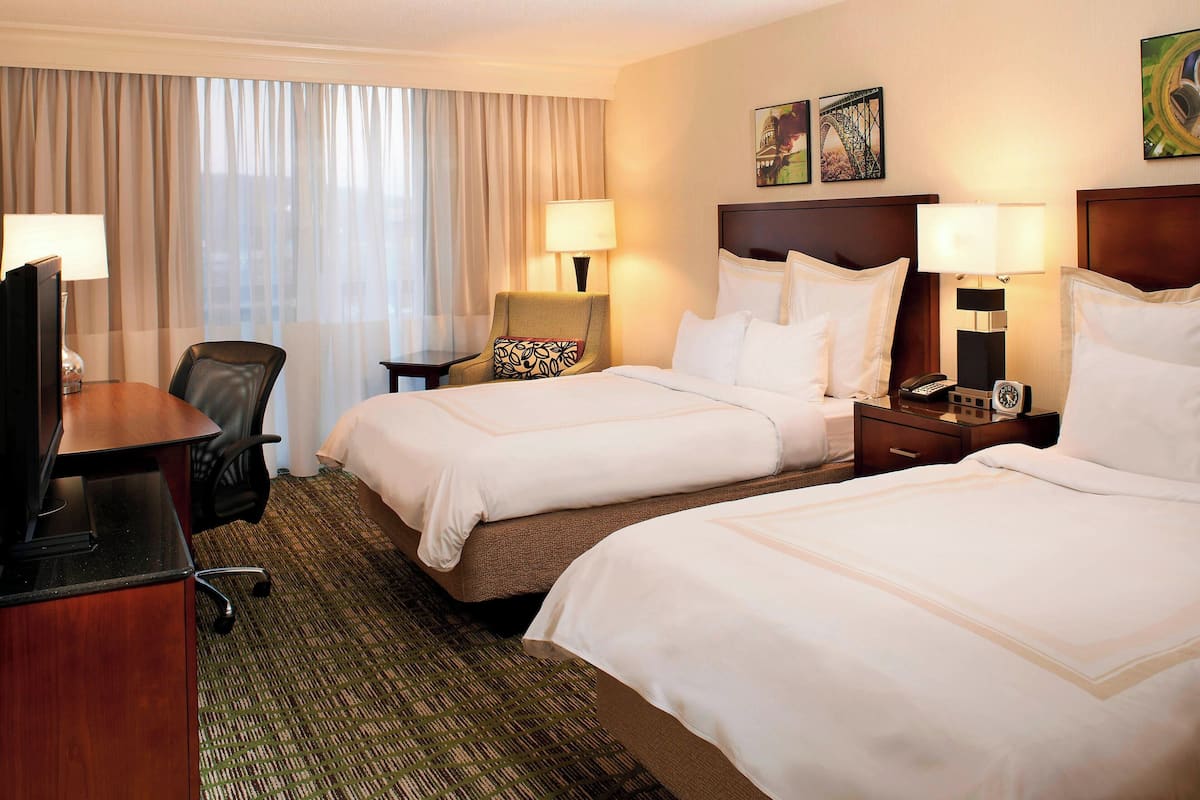 A hotel room with two beds, a desk, a chair, and a TV.