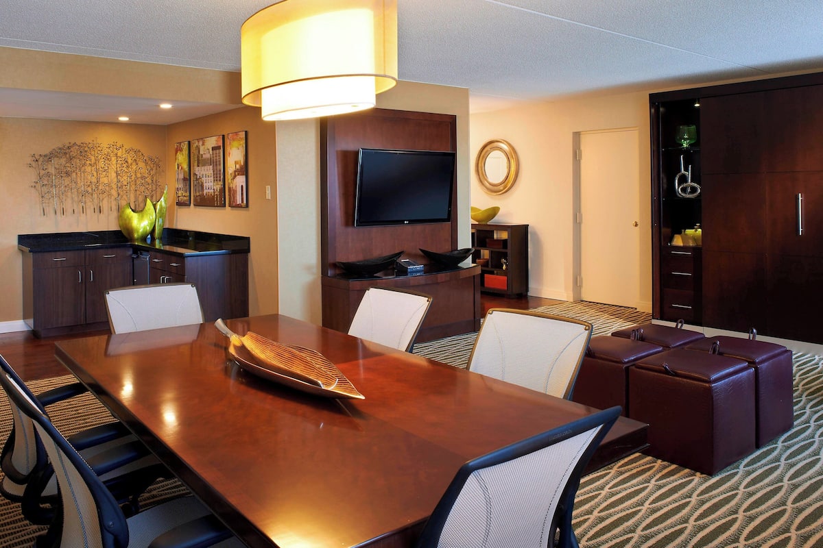 A hotel conference room with a large wooden table, several chairs, a television, and a minibar.