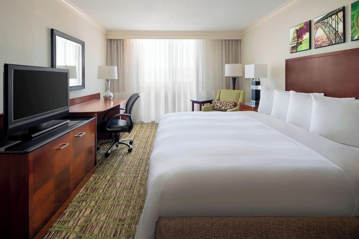 A hotel room with a large bed, a television, a desk with a chair, and a window with curtains.