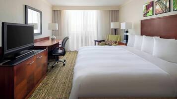 Una habitación de hotel con una cama grande, televisión, escritorio con silla y ventana con cortinas.