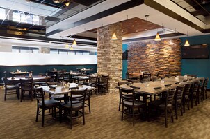 Un restaurante espacioso con numerosas mesas y sillas, una pared de acento de piedra e iluminación colgante.