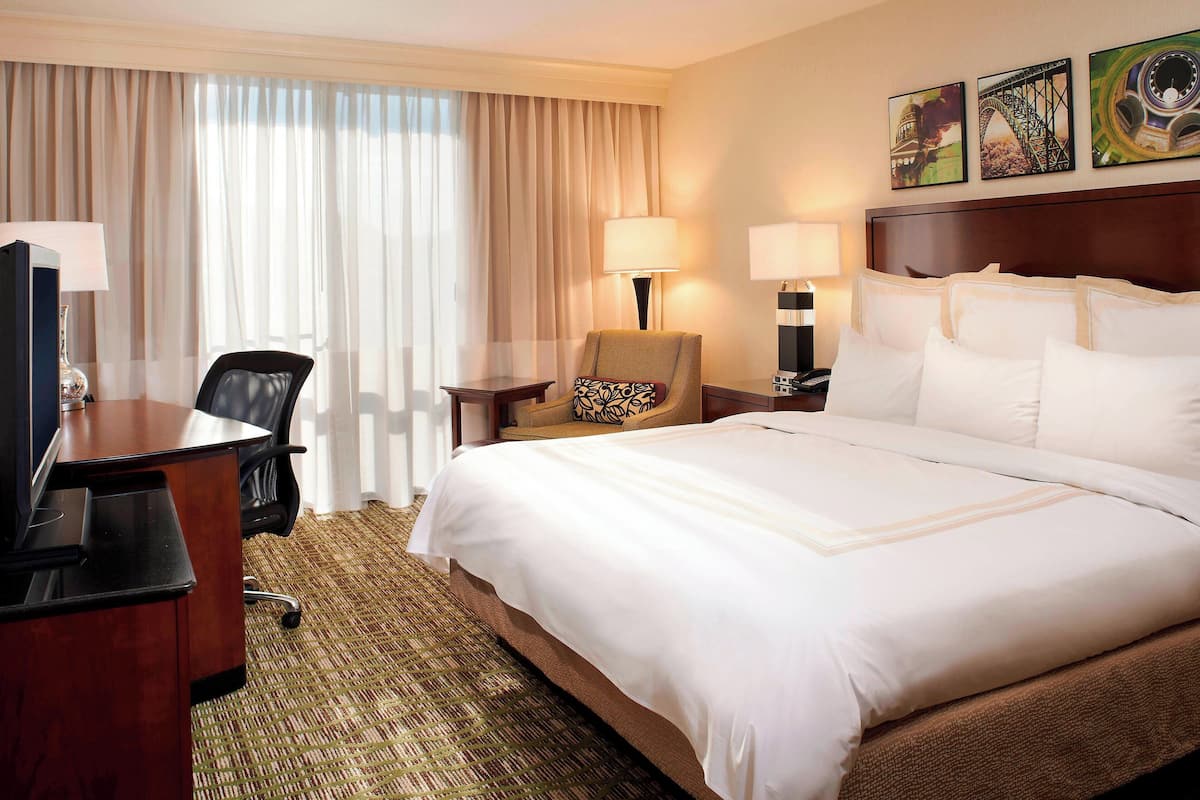 A hotel room with a large bed, a desk with a computer, a chair, and a lamp.