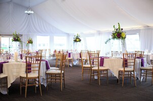 A tented event space with tables set for a reception, featuring white tablecloths and purple accents.