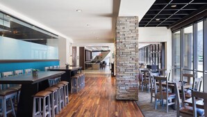 A modern restaurant interior with a long wooden bar, high ceilings, and large windows.
