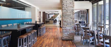 Ein modernes Restaurant mit langer Holztheke, hohen Decken und großen Fenstern.