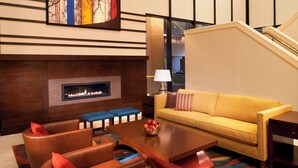 A modern living room with a fireplace, a sofa, two armchairs, a coffee table, and a staircase in the background.