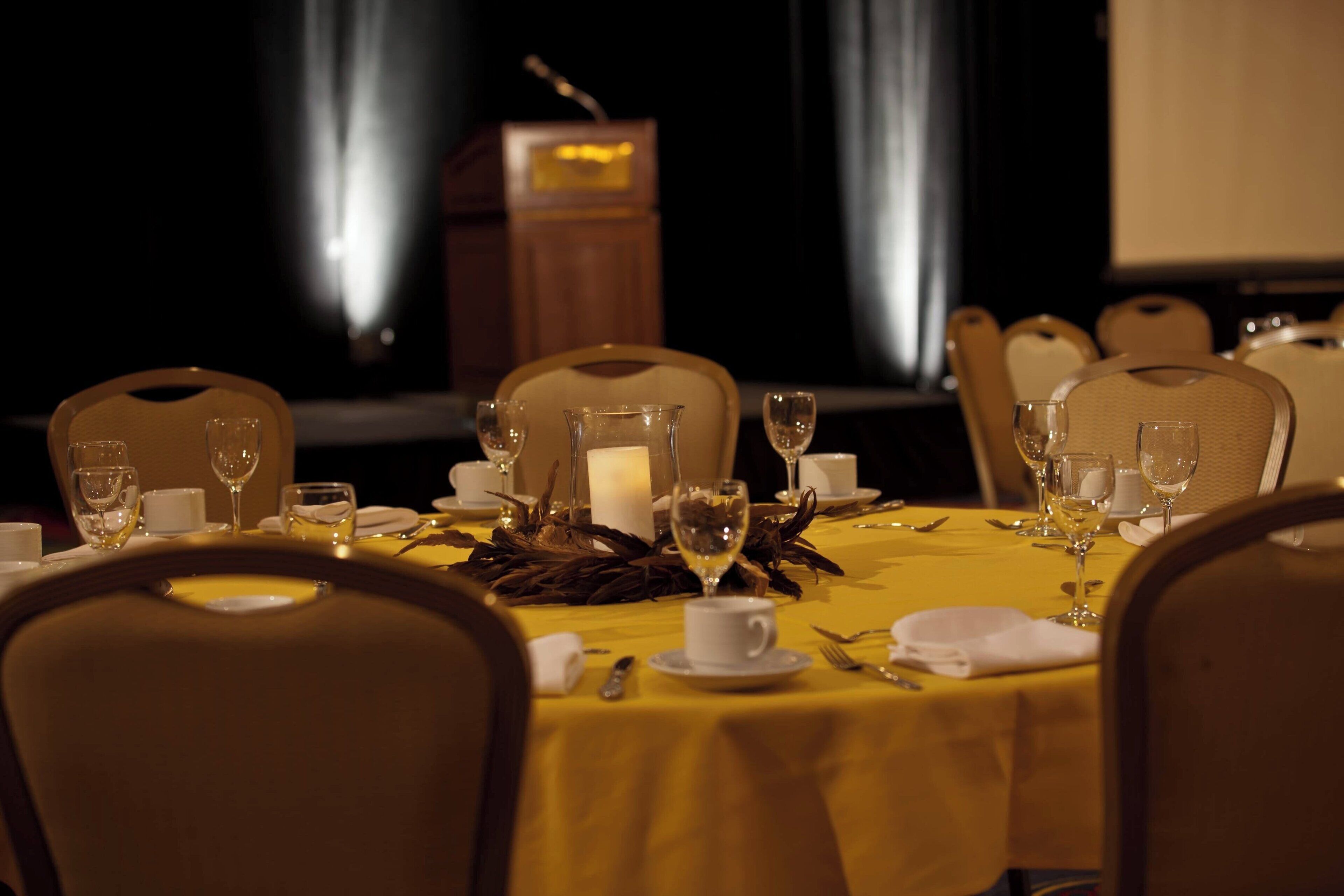 A dining table set for a formal meal with chairs, a candle centerpiece, and a podium in the background.