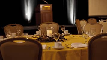 A dining table set for a formal meal with chairs, a candle centerpiece, and a podium in the background.