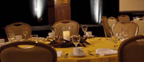 A dining table set for a formal meal with chairs, a candle centerpiece, and a podium in the background.