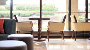A modern lobby with a sofa, two chairs, a small table, and a large window offering a view of greenery outside.