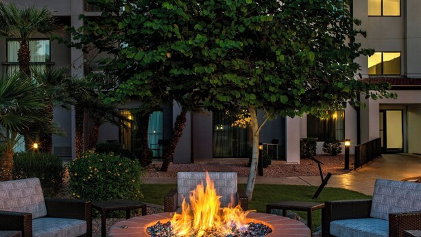 A circular fire pit with seating around it, surrounded by greenery and a building in the background. - Courtyard by Marriott Phoenix Airport (Phoenix)